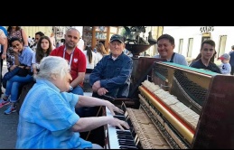 The grandmother sat in front of the piano on the street and played in such a way that people passing by gathered around her
